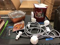 Overview photograph showing the Copper Chef cooking pot with glass lids on the left, the Waterpik shower head and hose coiled in the center, and the Victorian style music box on the right.