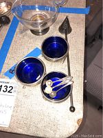 Photo of sterling silver salt servers with deep blue glass liners, candle snuffer, and heart glass bowl in sterling base shown on a table.