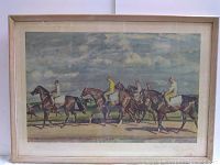 Framed print showing horse racing scene with jockeys on horses under cloudy sky.