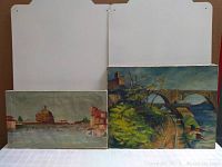 Two unframed landscape paintings side by side, one smaller with river and buildings, the other larger with bridge and tracks.