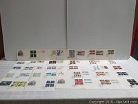 Wide view of multiple first day issue stamp covers and cards arranged on a white surface showing various designs and cancellation marks.