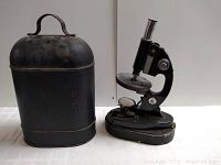 Microscope and its metal carrying case placed side by side showing the full items.