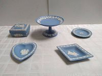 Five pieces of Wedgwood blue jasperware including a trinket box with lid, pedestal cake stand, round plate, heart-shaped dish, and square dish on white tablecloth