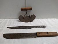 Top view of wooden handled mezzaluna chopper standing upright behind two knives, one long and narrow without handle and one cleaver style with wooden handle.