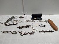 Top view of the entire lot showing multiple pairs of antique eyeglasses, a carved wooden case, a blue case with loose lenses, and a magnifying glass pendant.