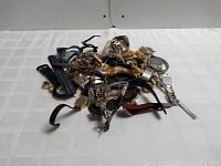 Top-down photo of 25 assorted wristwatches and watch parts piled together, showing variety of bands and watch faces.