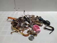 Pile of assorted watch parts including metal and leather bands, watch faces, and a pink rubber strap.