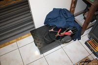 Black metal chest with diamond plate top, jumper cables on top, and blue coveralls hanging nearby