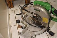 Photo showing entire miter saw with metal base, blade guard, and green handle.