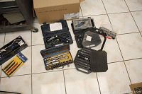 Wide view of the lot on tiled floor showing various socket sets, screwdriver bit sets, and a cordless screwdriver.