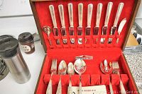 Full view of open wooden chest containing WM Rogers Bros flatware with red felt backing holding various flatware pieces in place.