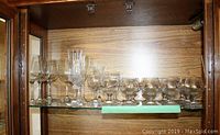 Shelf displaying various cut and stemmed glasses including tall and short glasses, some with etched or patterned designs.