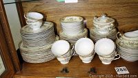 Photo showing stacked dinner plates, bowls, and cups with floral decorating and gold trim in a cabinet.