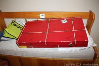 Closed red flatware case on sofa with some bags underneath
