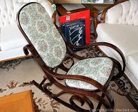 Full view of bentwood rocking chair showing floral upholstered seat and backrest, curved armrests, and curved wooden rocker base on floral carpet.