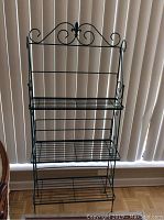 Full front view of the black metal bakers rack showing all three shelves and decorative top.