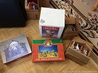 Three boxed nativity sets, a lit angel tree topper figure, and a boxed Santa angel figurine grouped together on floor.