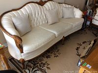 Full front view of the Victorian style three-seater couch with carved wood trim and two cream cushions on patterned carpet.