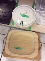 Ceramic tureen with lid and wooden cutting board underneath, showing metal handle on cutting board side