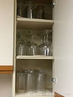 Shelving with assorted clear glassware including stemmed wine glasses, highball glasses, and small jars