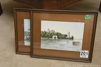 Two 8x11 inch framed watercolor paintings leaning against a chair, with brown mats and wooden frames