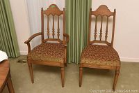 Photo of two Malcolm oak dining chairs side by side, one with armrests, both with ornate carved backs and upholstered seats.