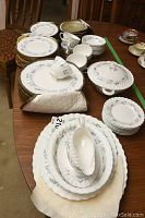 Overview of assorted white fine bone china pieces including plates, cups, gravy boat, serveware and quilted storage case on wood table.