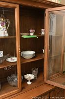 Glass cabinet with assorted glassware and china including plates, bowls, and a floral pitcher.