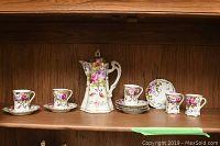 Full view of coffee pot, cups, and saucers arranged on shelf