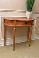 Front-side view of light brown veneer hall table showing single drawer with brass oval handle and tapered turned legs.