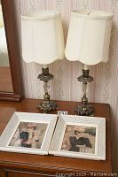 Two crystal and metal boudoir lamps with white fabric shades and two framed 8x10 prints on a wooden surface.