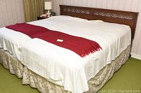 Two twin size beds placed side by side showing solid cherry wood headboards with carved geometric design, partially made up with white bedding and red runner.