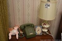 Vintage Northern Electric phone, floral china lamp, doll and clock on wooden table.
