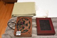 Photo of the artisan wooden purse with colorful floral and butterfly designs, next to folded fabric items on a blanket.