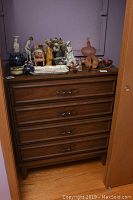 Full front view of the wood veneer dresser with decorative items on top, surrounded by closet doors.