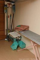Photo showing ironing board, mops, baskets, and dustpan set.