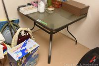 Photo of a 40x40 inch outdoor square table with a dark metal frame and tempered glass top, showing table surface and legs.