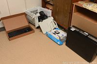 Wide view of the lot showing the VR3 wireless rear view camera system in its box, black briefcase upright, and other assorted items on floor and on a shelf.