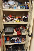 Front view of open Workforce resin cabinet showing cluttered contents including hand tools, rolls of tape, spray cans, hardware boxes, and power tools on multiple shelves.