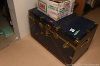 Side and top view of dark metal trunk with gold-colored hardware and a box on top.
