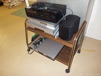 Photo showing Yamaha stereo receiver and two DVD players on top shelf of the rolling cart, with Denon speakers beside them.