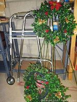 Aluminum walker with three artificial holiday wreaths, two on wire stands and one on the floor, showing whole lot.
