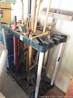 Mobile tool holder loaded with various long-handled garden tools including rakes and brooms, viewed from an angle showing tool handles and resting rack slots.