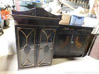 Full side view showing the black base cabinet with rooster artwork and drawers and the top hutch with glass doors and decorative top.