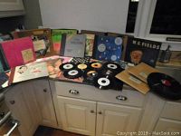 Wide view of vinyl record albums and 45 RPM singles laid out on a kitchen counter showing album covers and loose singles.