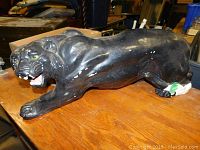 Black panther figurine on wooden table with visible scratches and chips seen on body and near base.