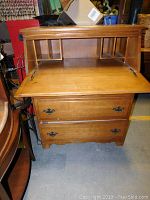 Wooden dresser with open fold-out desk showing small internal slots for organization, visible wear and wood grain.