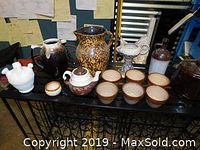 Assorted pottery pieces displayed on black shelving, including bowls, pitchers, teapot, decorative hen shape and bottle.
