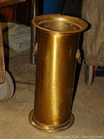 Front angle of the tall brass umbrella holder showing its cylindrical shape and one decorative lion head handle.