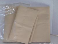 Beige-colored folded fabric drape with visible stitching, showing part of the packaging beside it.
